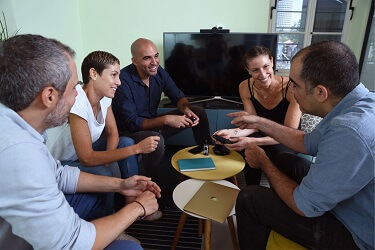 People are sitting and smiling in front of a round table, one of them holding the Lumen device and talking